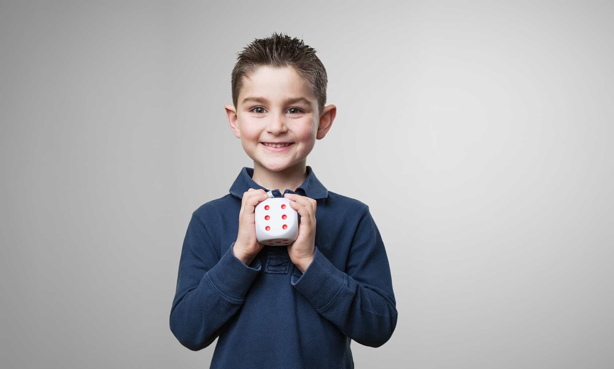 Boy-holding-large-dice Volunteer in school with numeracy using creative activities to help primary school child gain skills and confidence in maths.
